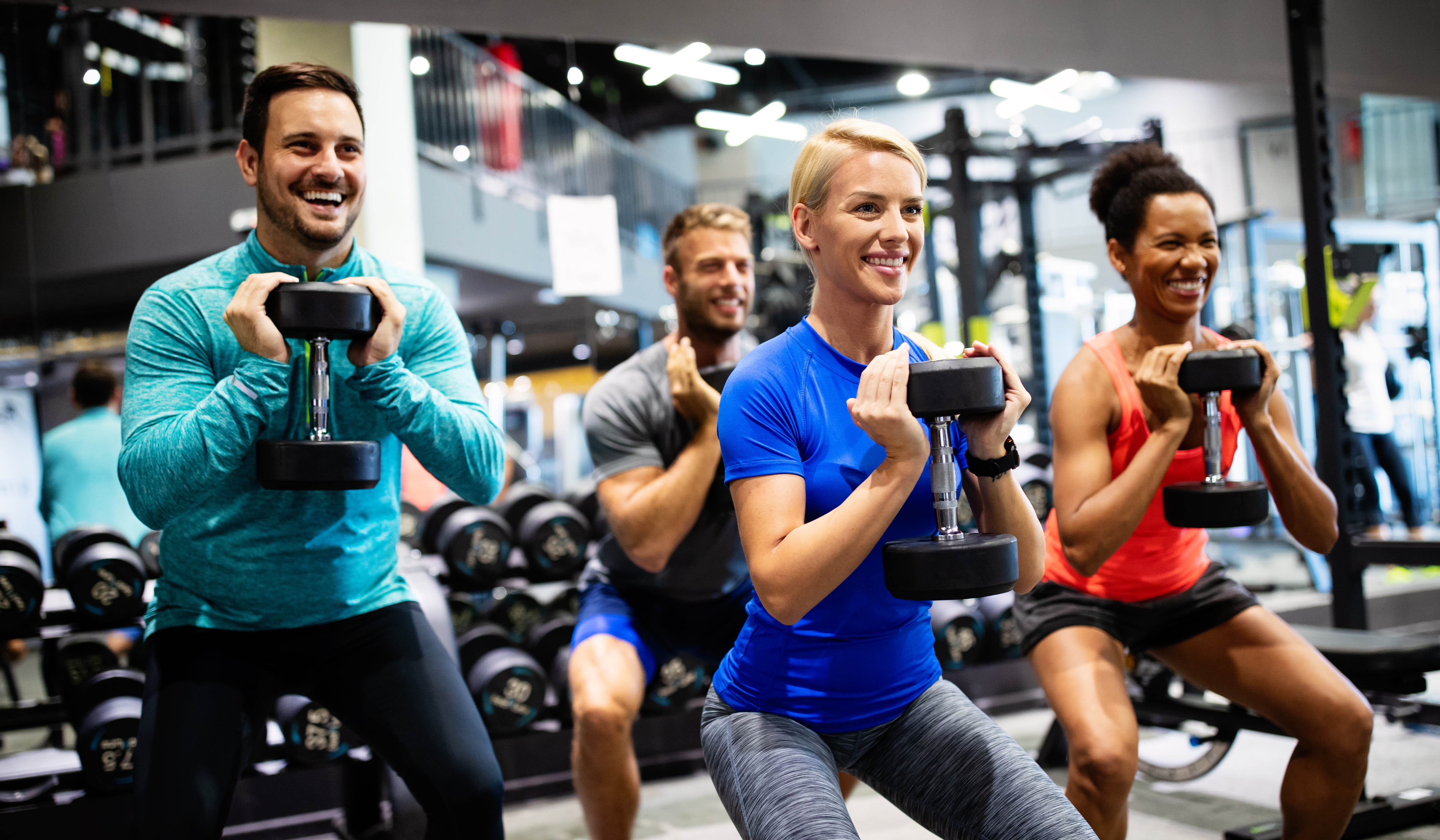Multi-racial group of young men and women doing dumbbell squats in the gym